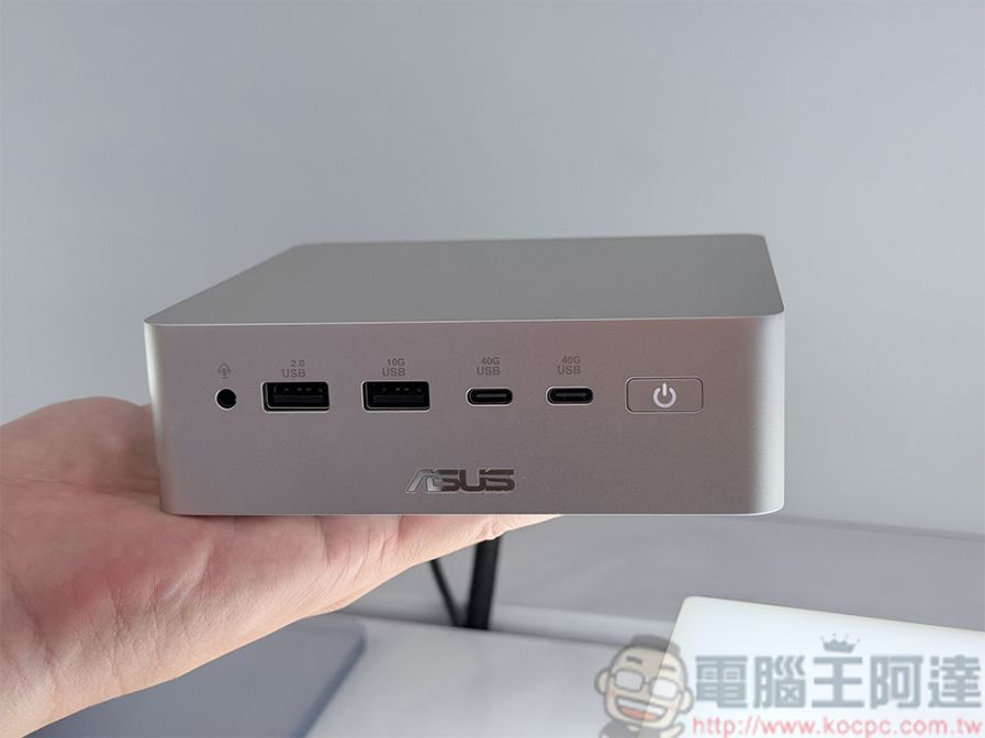 Bir el, gümüş renkli, kare şekilli bir ASUS mini bilgisayarı tutuyor. Ön panelde soldan sağa doğru bir kulaklık simgeli jak girişi, '2.0 USB', '10G USB' ve '40G USB' yazılı birer USB bağlantı noktası, '40G USB' yazılı bir USB-C bağlantı noktası ve güç simgeli bir güç düğmesi yer alıyor.