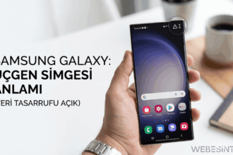 Bir elinde Samsung Galaxy akıllı telefon tutan kişi; ekranın sağ üst köşesinde veri tasarrufunun açık olduğunu gösteren, içinde yukarı ve aşağı oklar bulunan üçgen simgesi daire içine alınarak vurgulanmış. Görselin solunda "SAMSUNG GALAXY: ÜÇGEN SİMGESİ ANLAMI (VERİ TASARRUFU AÇIK)" yazısı bulunuyor.